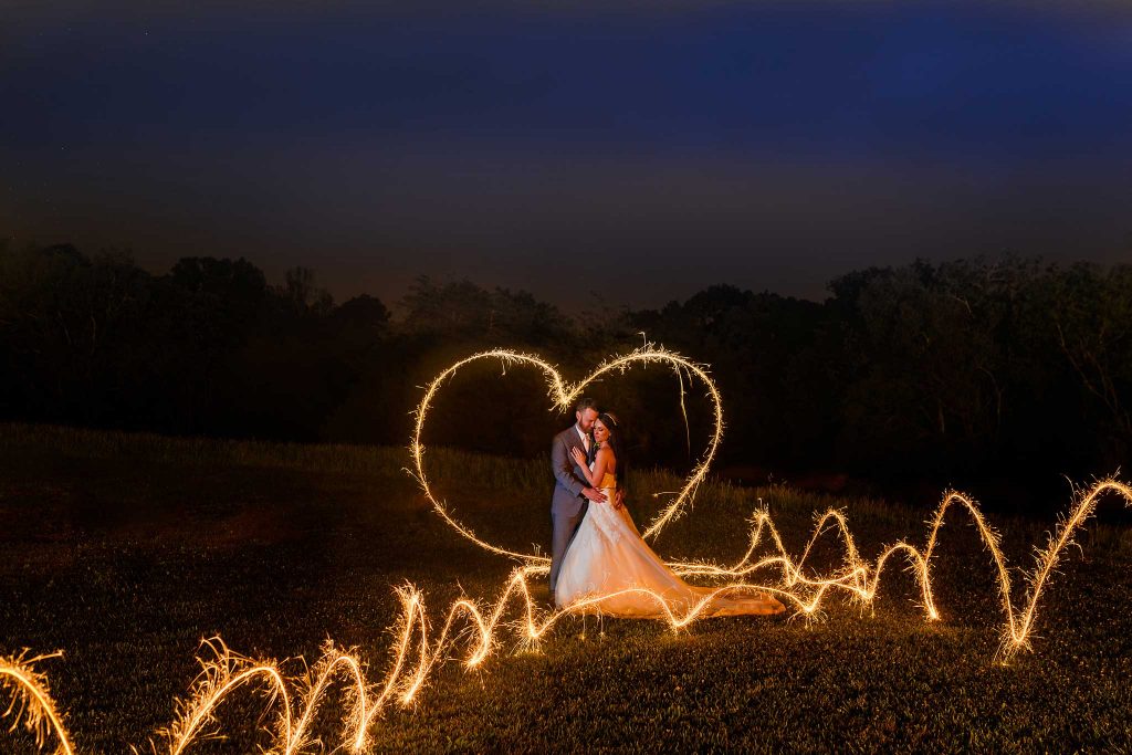 bride and groom with sparkler drawn heart and flames around them in the dark at The barn at drewia hill