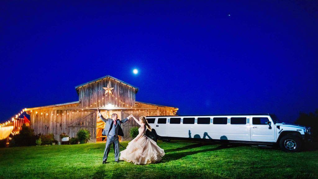 couple dancing at night in front of The barn at Drewia Hill with a white stretch Hummer Limo and barn venue